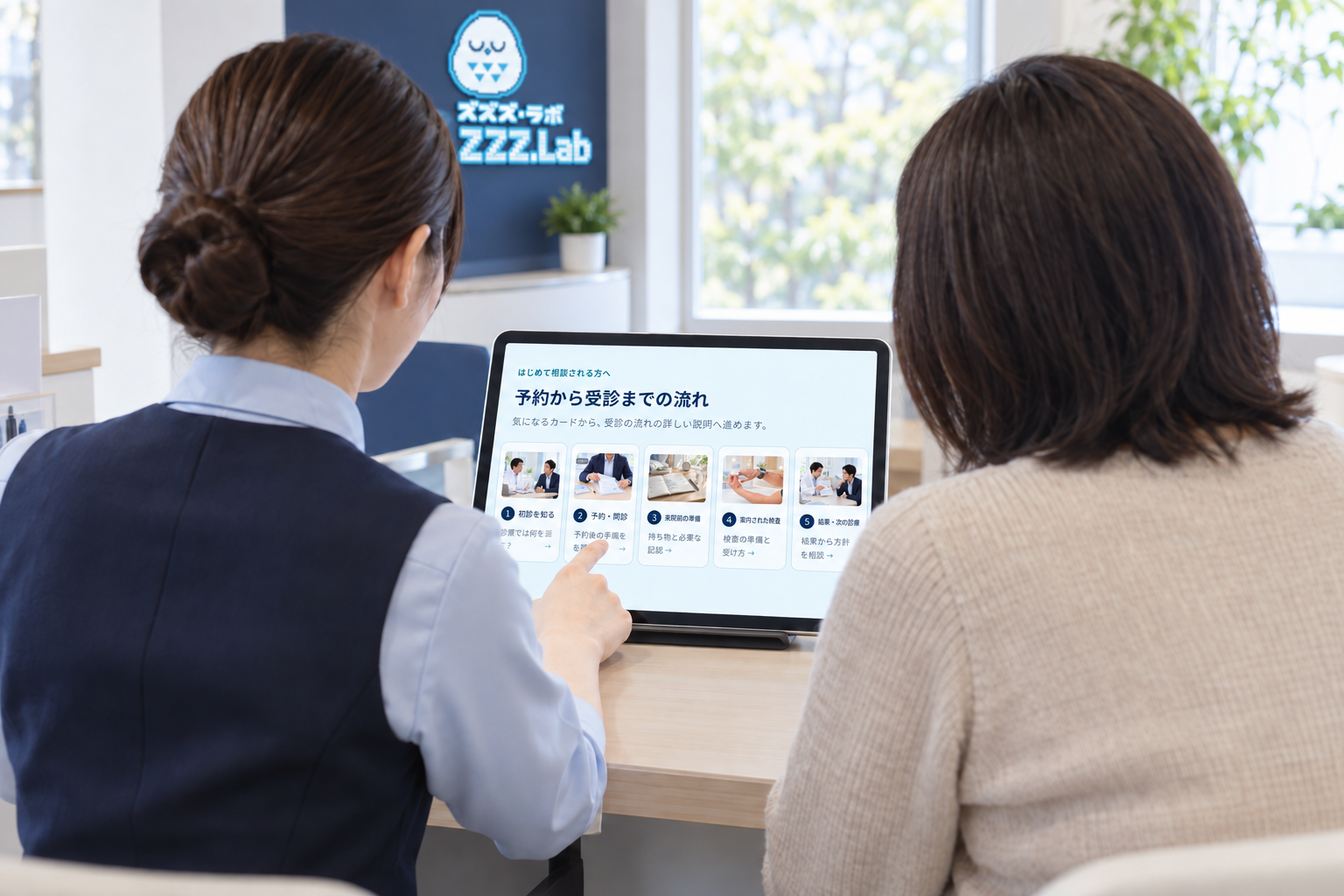 患者さんと受付スタッフが、同じタブレットの説明資料を確認する後ろ姿